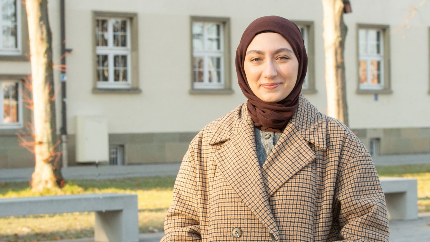 Die Studentin Merve Akpinar steht vor einem Gebäude am Eingang des Campus der JGU und schaut in die Kamera, Fotograf: Peter Pulkowski