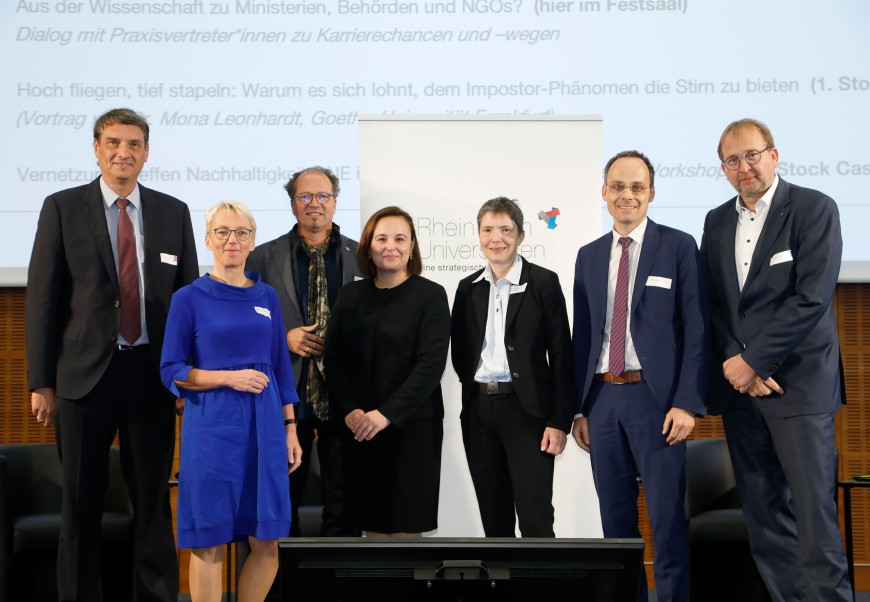 Präsident:innen und Vizepräsidentinnen der RMU sowie Staatssekretärin Asar und Staatssekretär Alt stehen vor RMU-Bannern