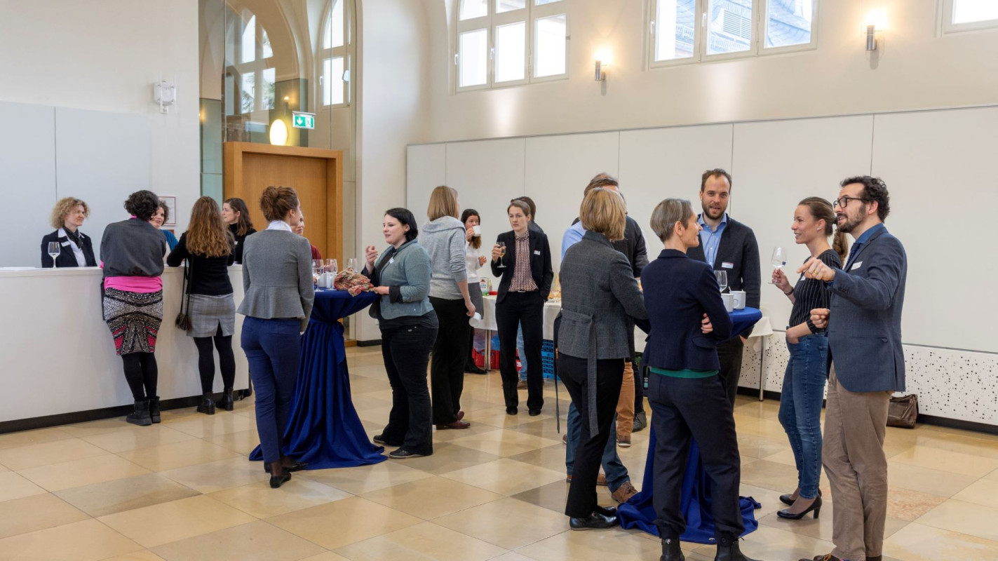 Profesor*innen an Stehtischen sind in Gesprächen vertieft