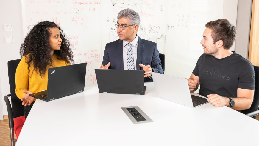 Professor Ahmad-Reza Sadeghi sitzt mit Laptop und zwei weiteren Personen mit Laptop am Tisch und spricht. Bild: Klaus Mai