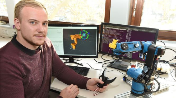 Studierender vor Rechner und mit Roboter
